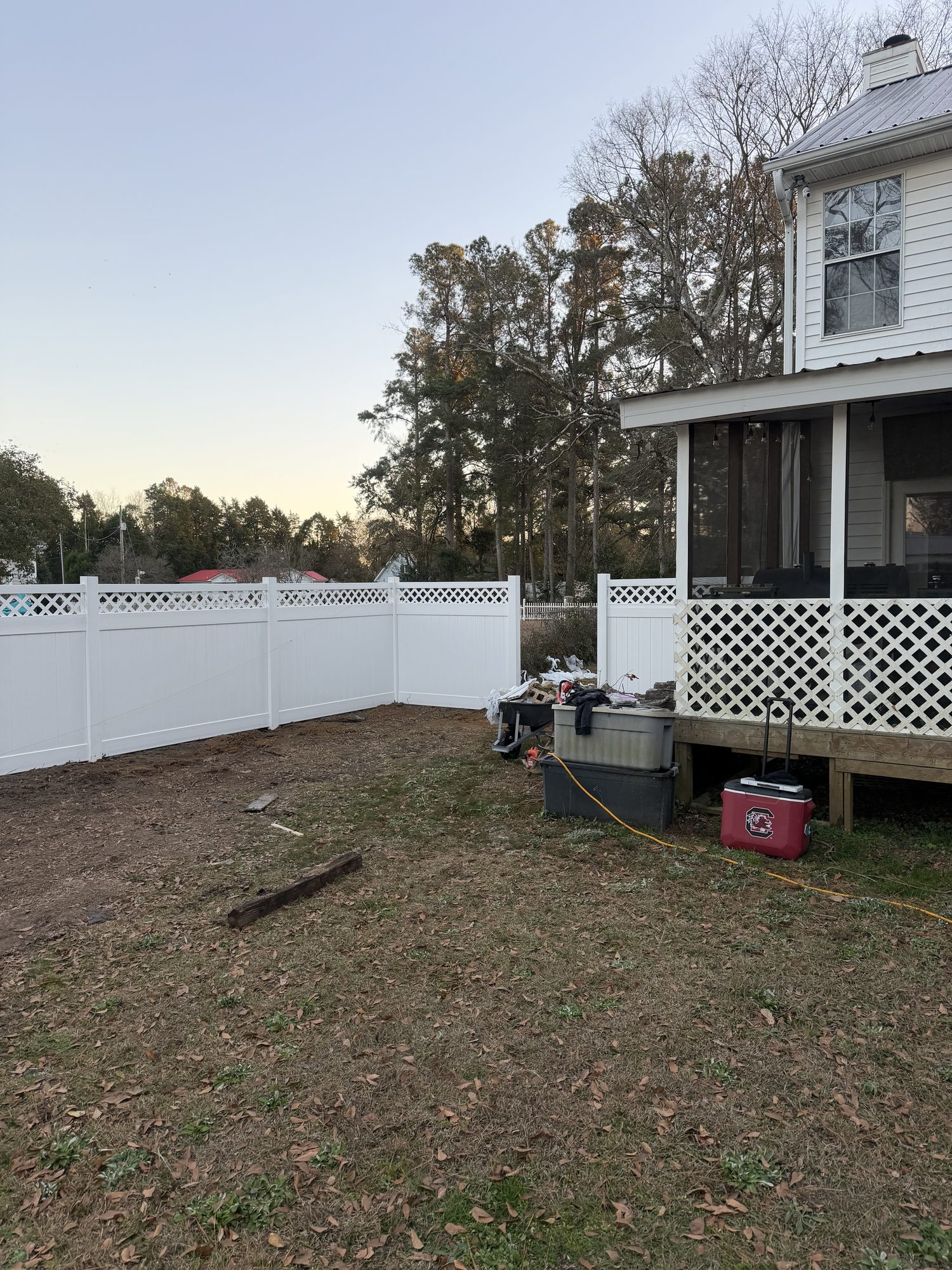 Newly installed white vinyl privacy fence with lattice trim bordering residential backyard during yard preparation phase.