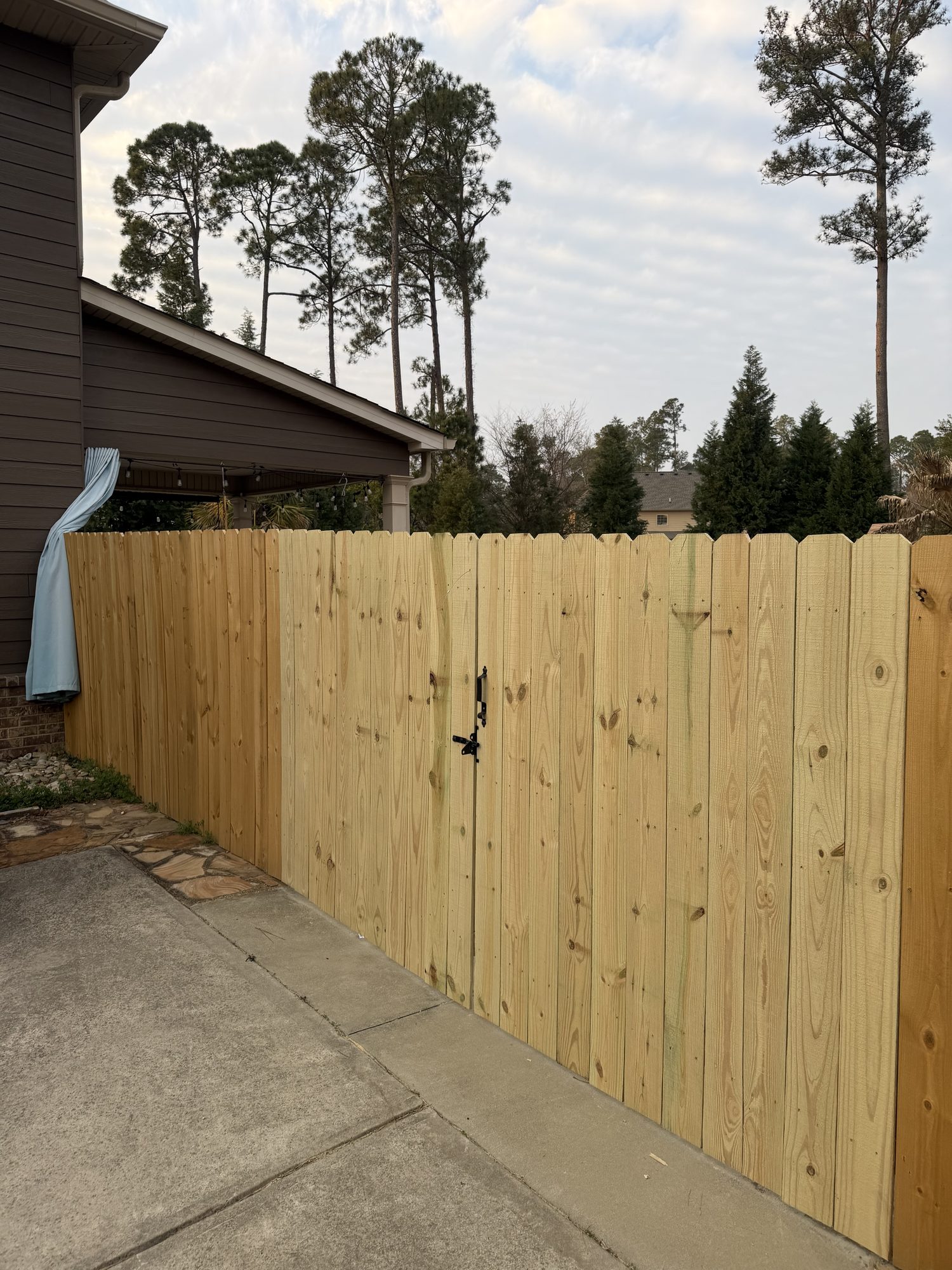 Newly installed wood privacy fence with vertical pine boards and black gate latch along residential driveway in CSRA area.