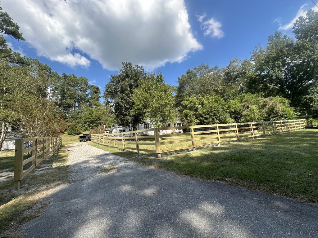 Wooden post and rail farm fence with gate along a rural driveway