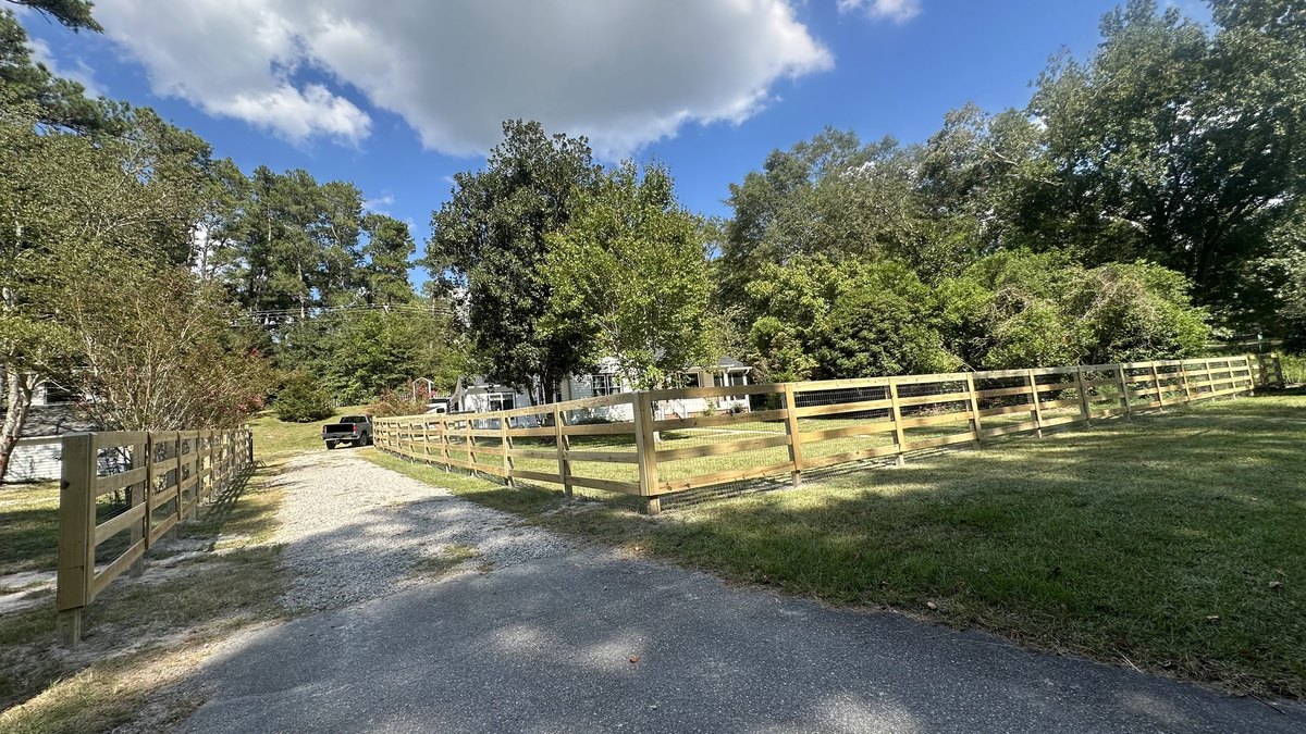 Wooden post and rail farm fence with gate along a rural driveway