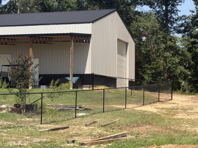 Black chain-link fence securing a rural property with modern agricultural building and covered porch structure.