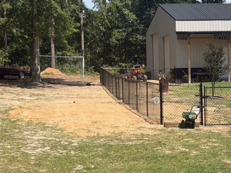 Black chain link fencing securing a rural farm property with modern gray barn and equipment storage areas in the CSRA.