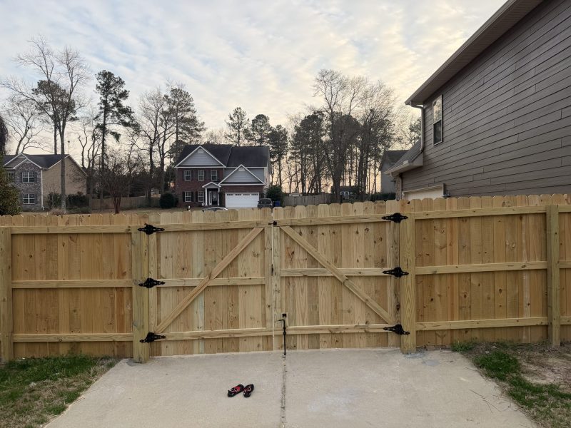 Completed wooden driveway gate installation with black hardware across residential concrete driveway in suburban CSRA neighborhood.
