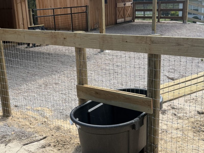 Farm fencing installation with wooden paddock enclosure, metal gates, and water trough for equestrian property in rural CSRA area.