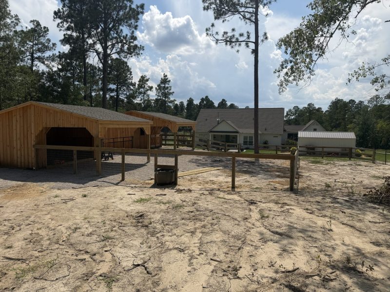 Farm paddock with wooden fencing, tan metal barn structures, and sand arena typical of equestrian properties in rural CSRA.