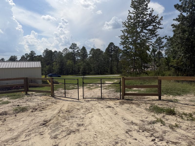 Farm property with wooden and metal gates across driveway, barn, and pasture fencing for livestock management.