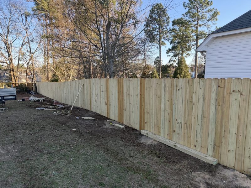 Newly installed wood privacy fence with tan vertical planks and horizontal support beams along residential property line in Aiken area.