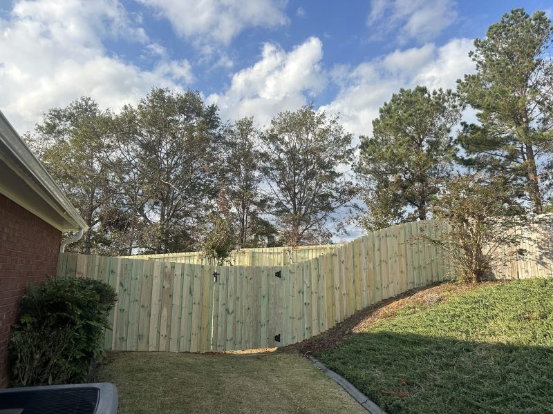 Light-colored wood privacy fence installed in residential backyard with mature trees and lawn.