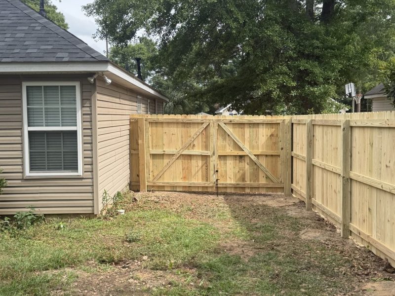 Natural pine wood privacy fence with centered double gate installed around residential backyard in Aiken area.