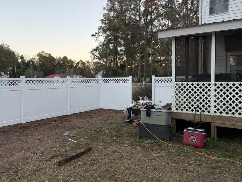 Newly installed white vinyl privacy fence with lattice trim bordering residential backyard during yard preparation phase.