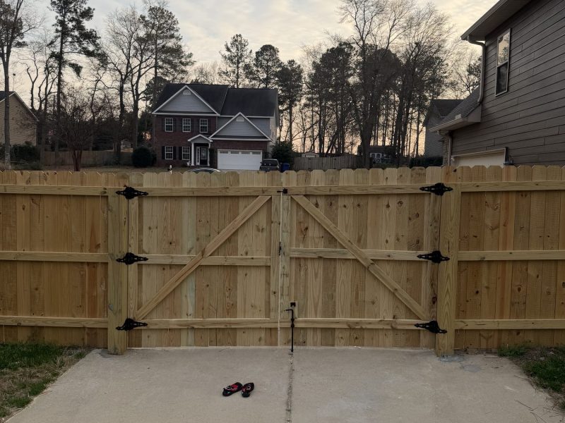 Newly installed wood driveway gate with X-braced panels and black hardware in residential Aiken area neighborhood.