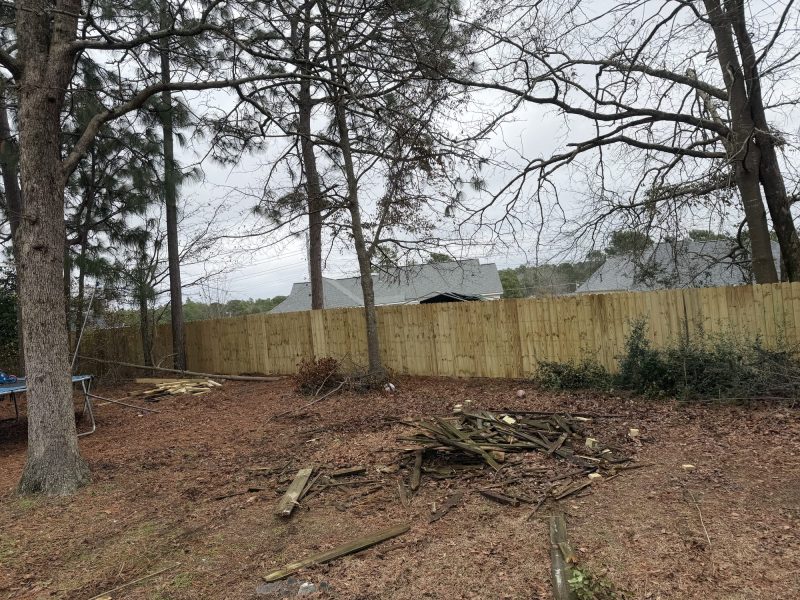 Newly installed wood privacy fence in residential backyard with cleared grounds and surrounding trees.