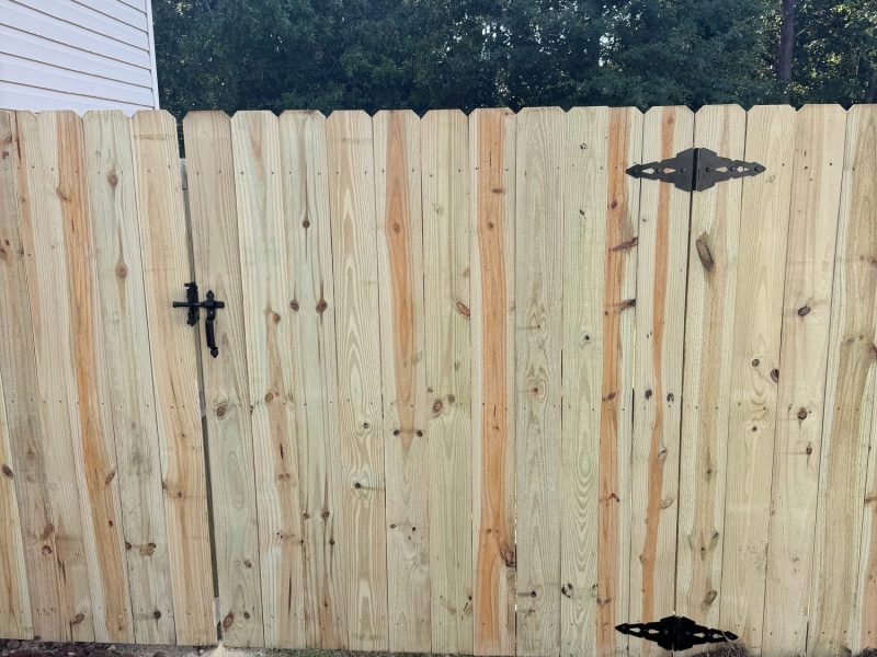 Newly installed wood privacy fence with light pine planks and black hardware gate hinges in Aiken residential property.