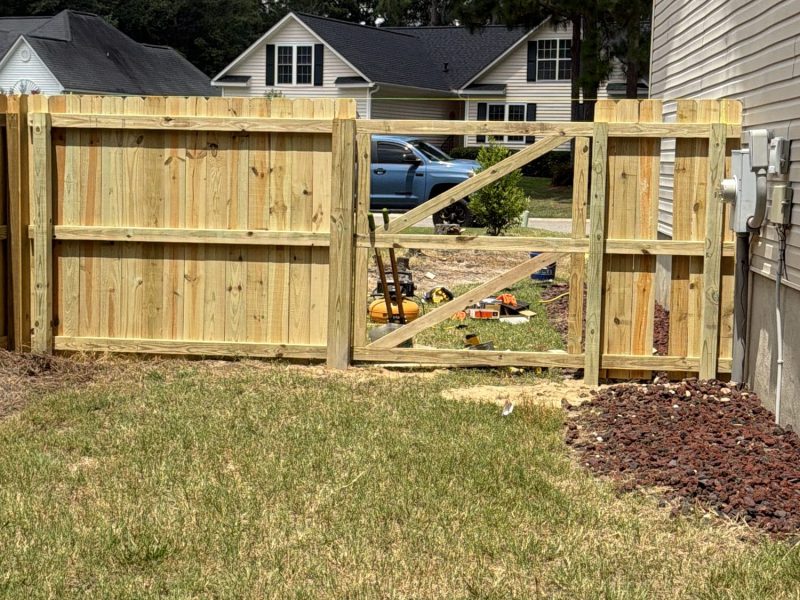 Newly installed wood privacy fence with solid tan panels and vertical slats surrounding residential backyard with gate entry and mulch landscaping.