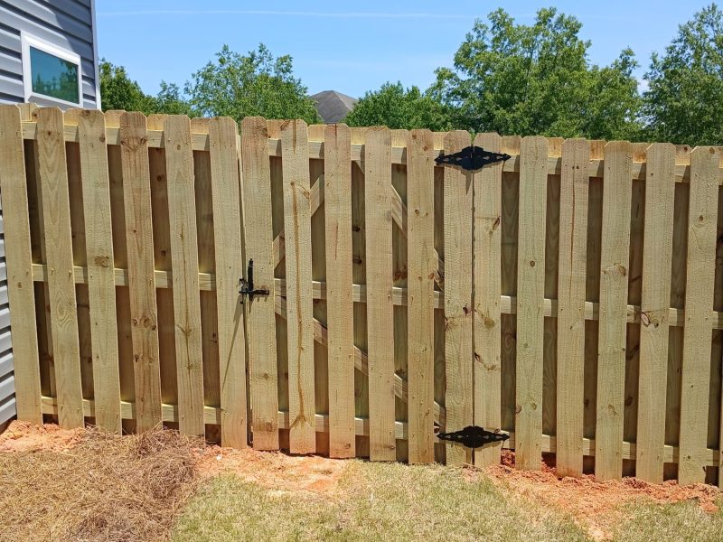 Newly installed wood privacy fence with vertical pickets and black metal gate in residential backyard.
