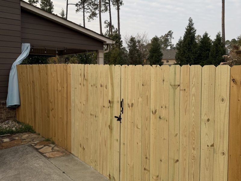 Newly installed wood privacy fence with vertical pine boards and black gate latch along residential driveway in CSRA area.
