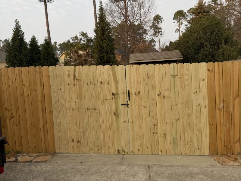Newly installed wood privacy fence with vertical planks and centered gate along driveway in residential CSRA neighborhood.