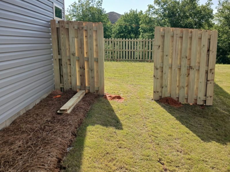 Pair of wooden privacy fence gates installed at residential backyard entrance with mulched landscaping and mature lawn.