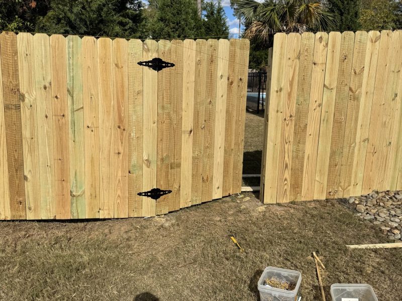Professional installing wooden privacy fence with vertical planks and black hardware in residential backyard.