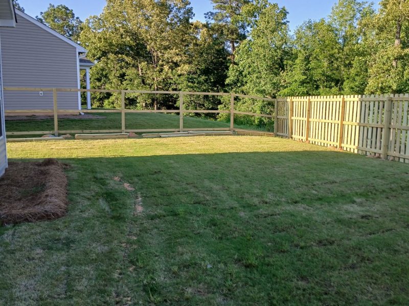 Residential backyard with newly installed wood privacy fence bordering fresh landscaping and lawn preparation.