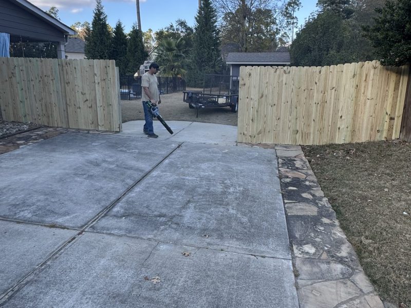 Residential property with completed wood privacy fences flanking a concrete driveway during post-installation site cleanup.