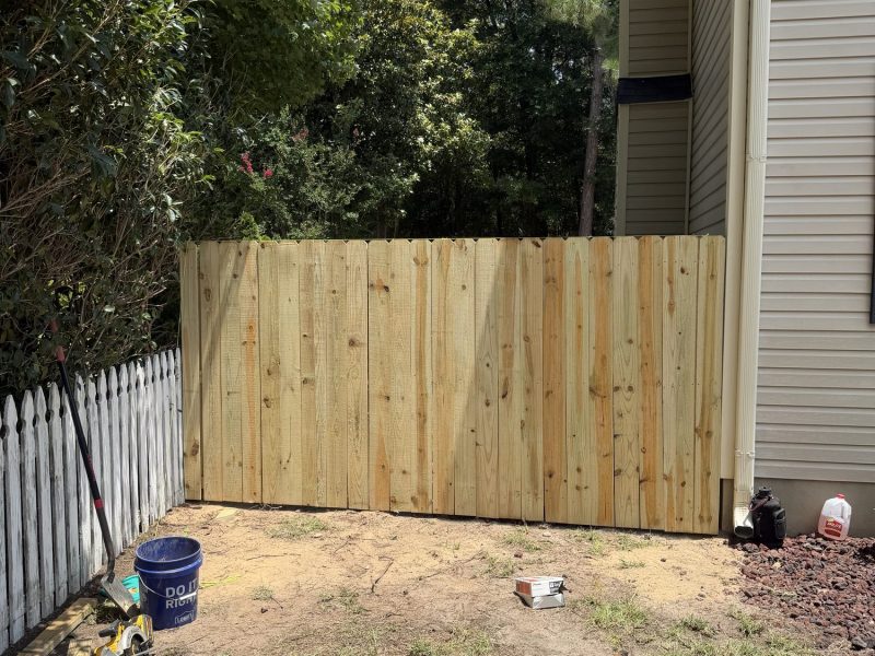 Residential wood privacy fence installation in progress showing vertical plank construction with tools and materials in backyard work area.