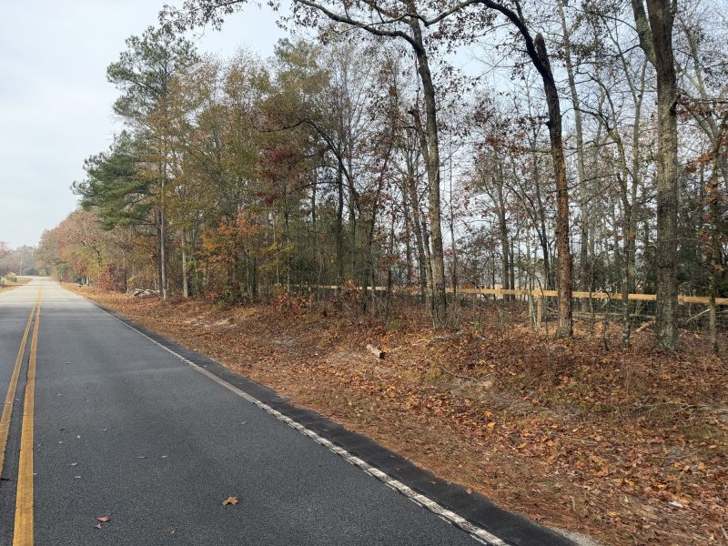Rural property entrance with post-and-rail fence boundary marking along tree-lined driveway in CSRA region.