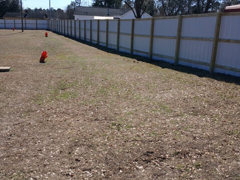 White composite privacy fence enclosing pet exercise area with wooden posts and gravel base.