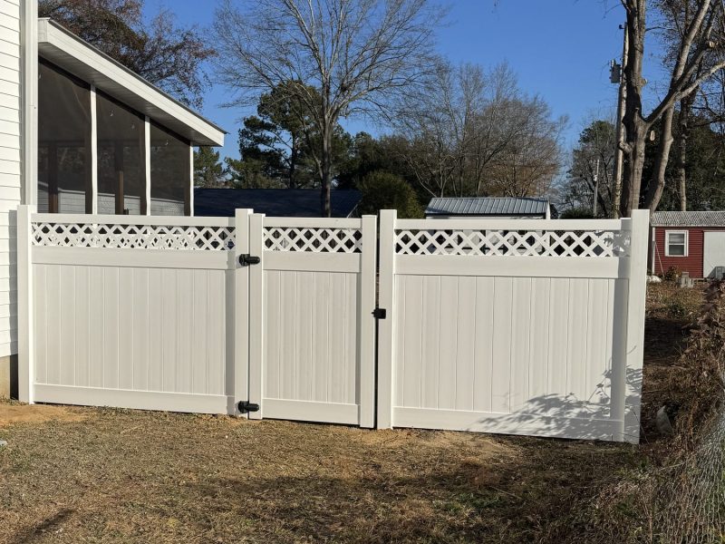 White vinyl privacy fence with decorative lattice top and matching gate installed in residential yard.