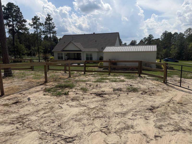Wooden and metal rail fencing for rural farmstead with livestock paddock and pine tree surroundings.