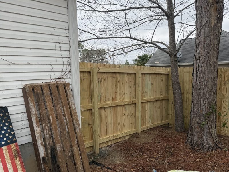 Wooden privacy fence installation in residential backyard with construction materials and equipment staged during active fencing project.