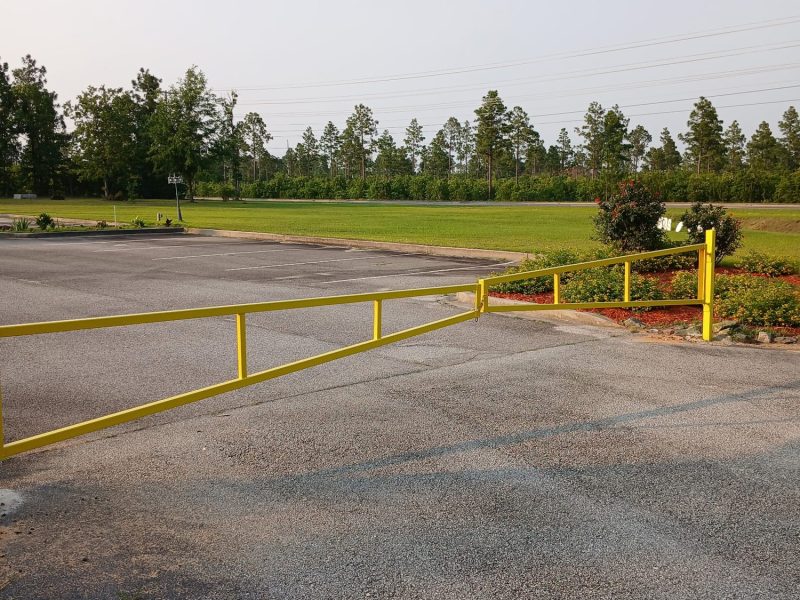 Yellow metal gate at rural property entrance with chain link fencing bordering open grounds and tree line.